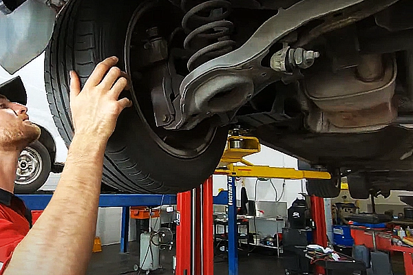 Mechanic checks suspension under car for a service check